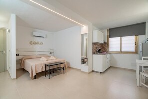A compact room with a bed, a small table, a kitchenette, and a window. - Domo Le Mura Puniche (Olbia)