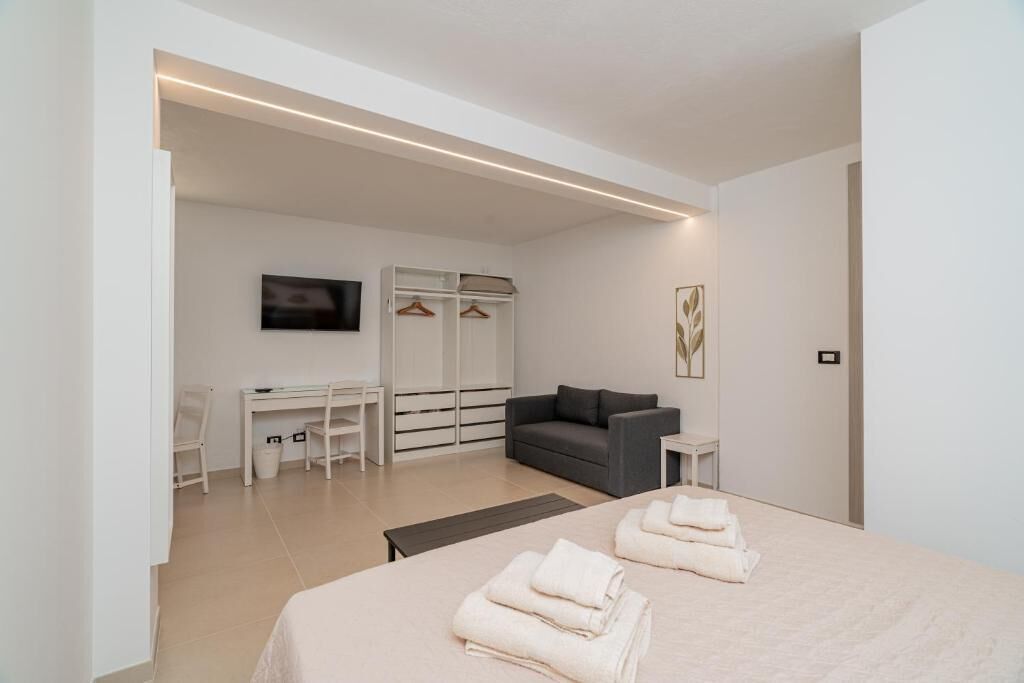 Ein modernes Schlafzimmer mit einem Bett, einem Schreibtisch, einem grauen Sofa und einem Fernseher.