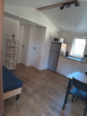A compact living space with a kitchenette, a dining area with a table and chair, a bookshelf, and a door leading to another room.