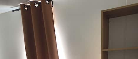 A bedroom with two beds, a wooden shelf unit, and a window with curtains.