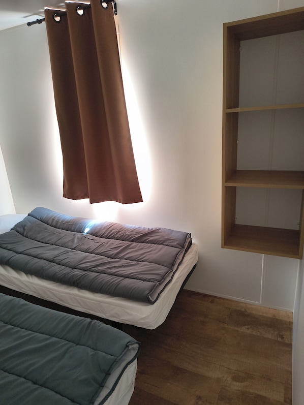 Un dormitorio con dos camas, una estantería de madera y una ventana con cortinas.