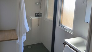 Une petite salle de bain compacte, équipée d’une douche, de toilettes et d’un lavabo. Une fenêtre laisse entrer la lumière naturelle et une serviette est suspendue sur un porte-serviettes.