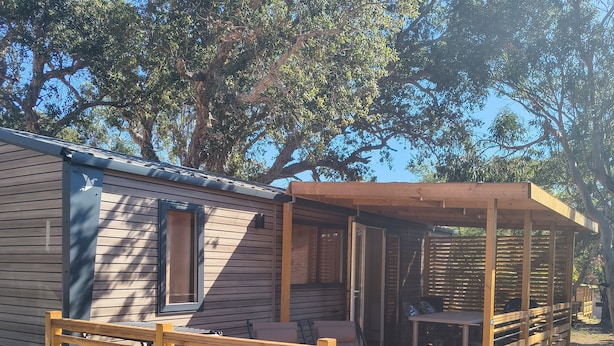 Une terrasse en bois avec un banc et une table, un patio couvert et une maison mobile avec une fenêtre.