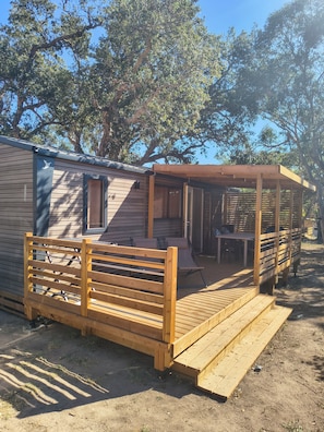 Una terraza de madera con un banco y una mesa, un patio cubierto y una casa móvil con ventana.