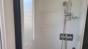 Un petit espace de douche fermé, doté d’une porte, d’un pommeau de douche et d’un panneau de commande.