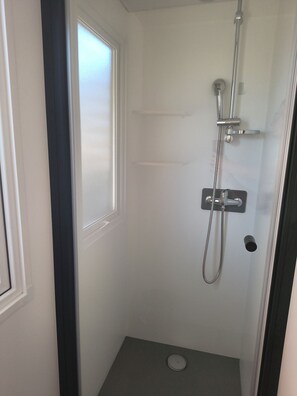 Un petit espace de douche fermé, doté d’une porte, d’un pommeau de douche et d’un panneau de commande.