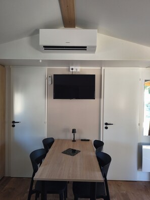 Une salle de conférence avec une table en bois, quatre chaises, un téléviseur fixé au mur et un appareil de climatisation au plafond.