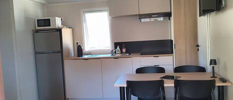 A compact kitchen with a refrigerator, microwave, and a small dining area with a table and chairs.