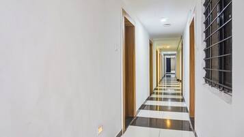Un couloir dont le sol est recouvert d’un motif à carreaux, menant à une pièce dotée d’une fenêtre.