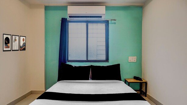 Una habitación con cama, ventana con cortinas, aire acondicionado de pared, mesita de noche con teléfono y tres cuadros enmarcados en la pared.