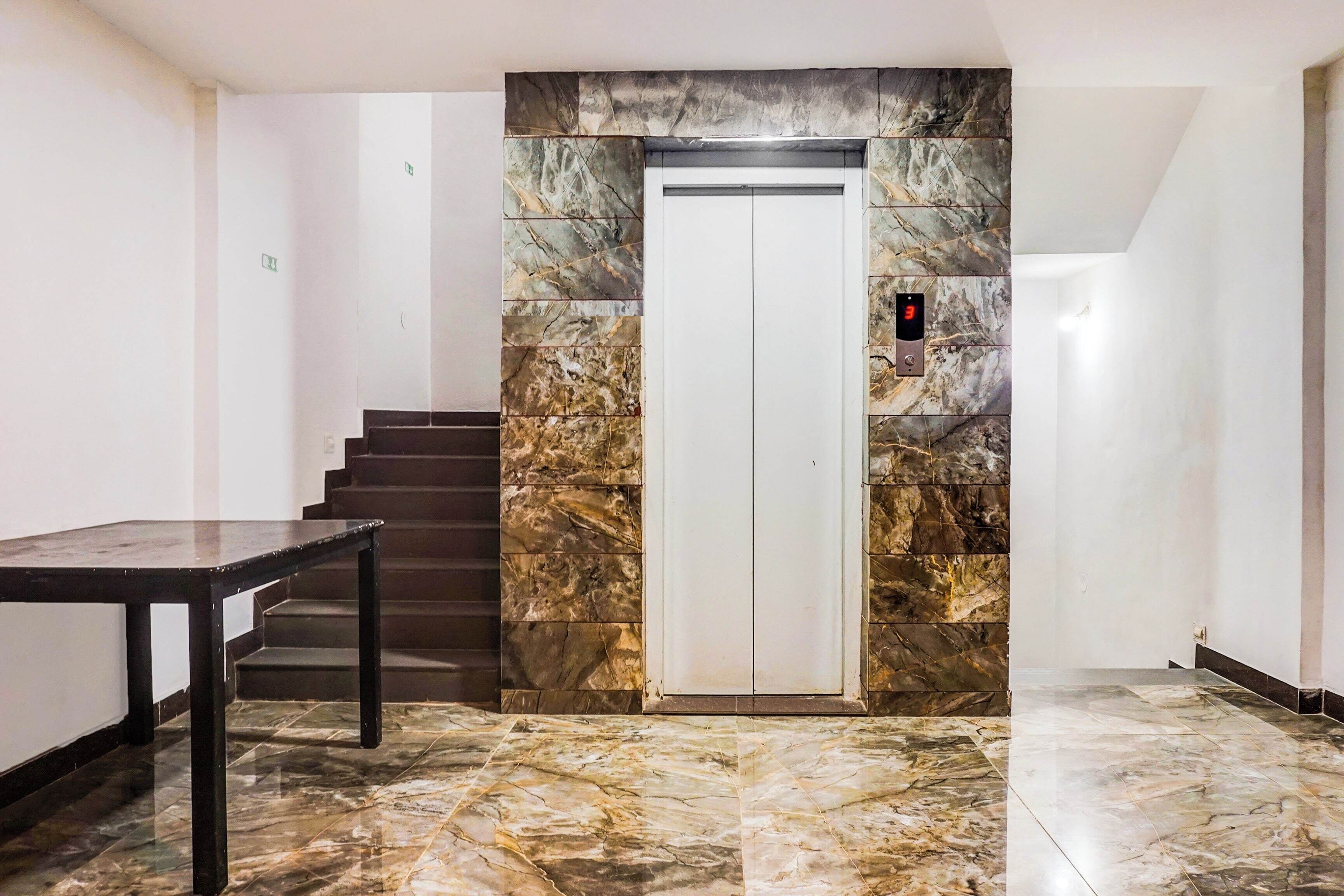 A hallway with a marble floor, a staircase, and a door with a digital elevator display.
