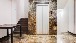 Un pasillo con piso de mármol, una escalera y una puerta con panel digital de ascensor.