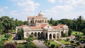 Un edificio grande e histórico con varios arcos y una cúpula, rodeado de jardines y senderos bien cuidados.