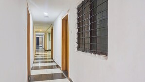 Un pasillo con piso a cuadros, una ventana con rejas y una puerta a la derecha.