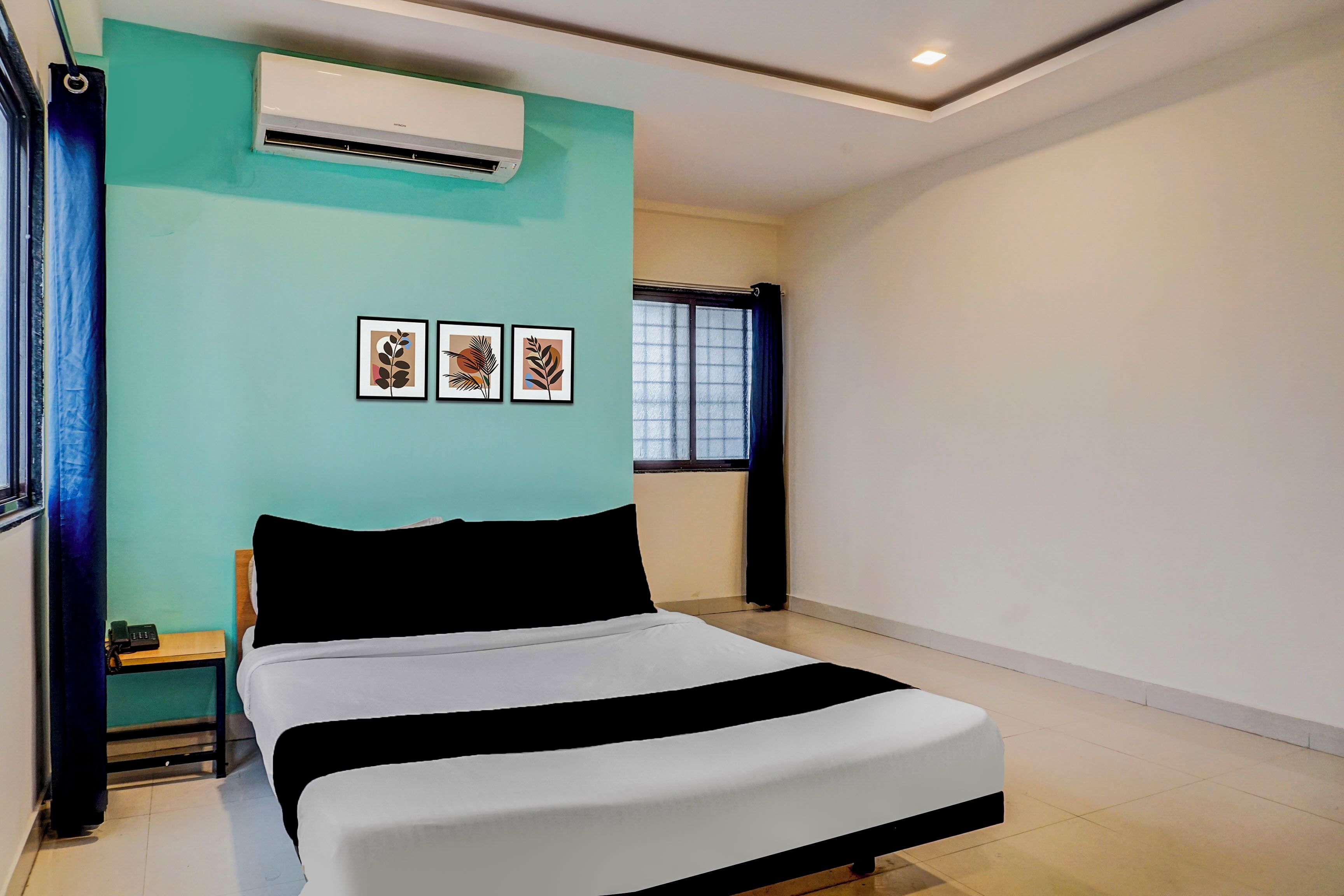 A bedroom with a bed, an air conditioning unit, a window with curtains, and three framed pictures on the wall.