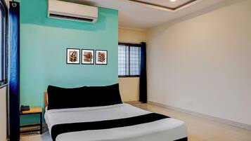A bedroom with a bed, an air conditioning unit, a window with curtains, and three framed pictures on the wall.