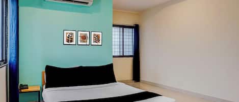 Un dormitorio con una cama, un equipo de aire acondicionado, una ventana con cortinas y tres cuadros en la pared.