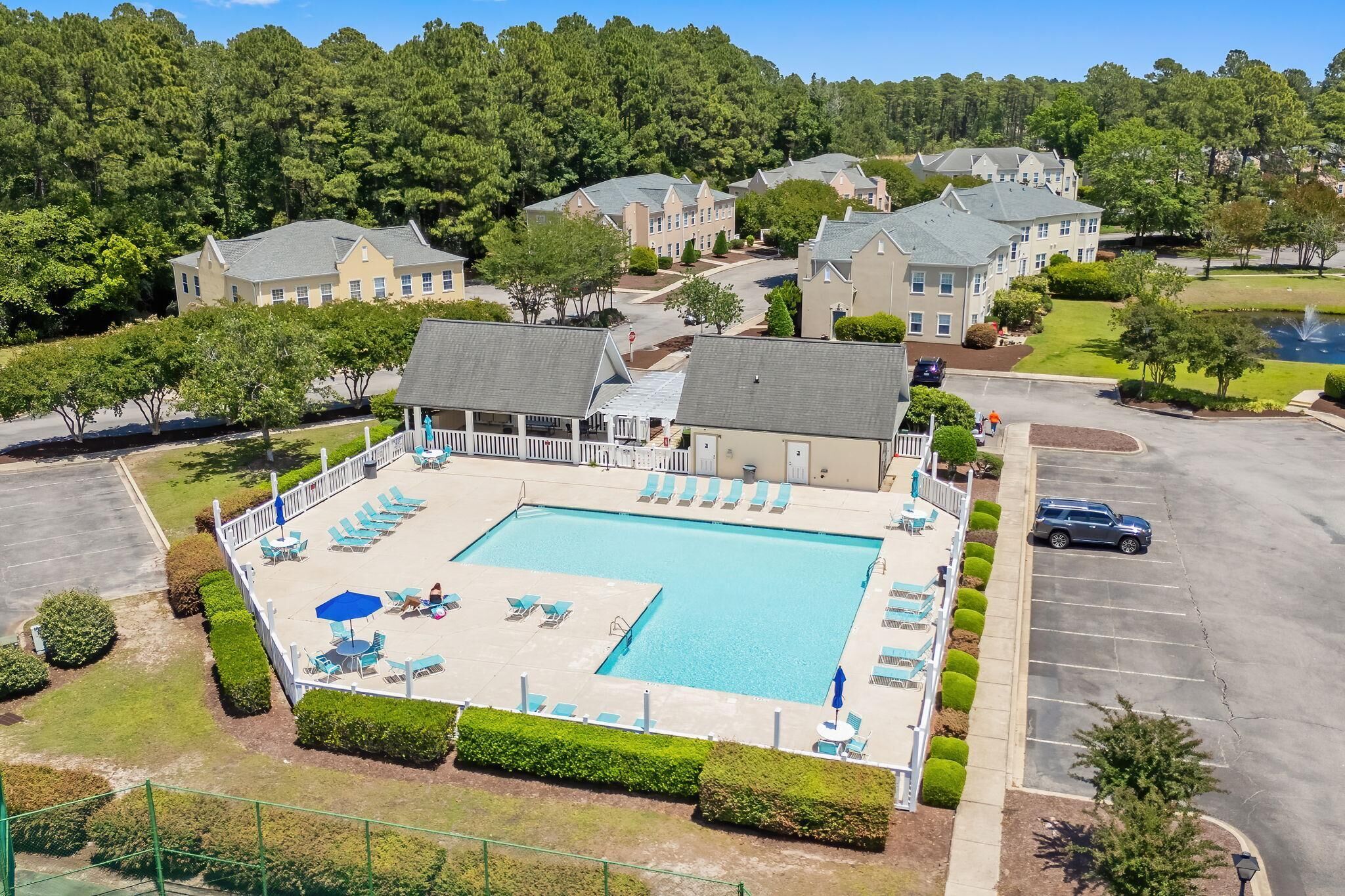 A swimming pool with lounge chairs and umbrellas, surrounded by a fence and greenery.