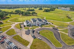 A golf course with a clubhouse, parking area, and a body of water in the background.