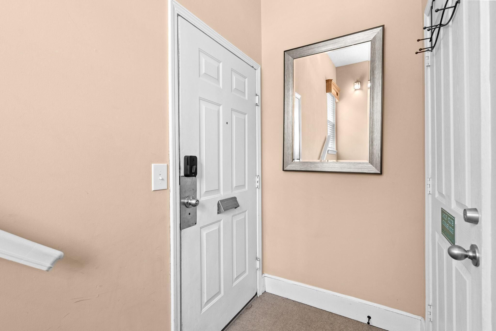 Un pasillo con una puerta blanca, un espejo en la pared y un perchero.