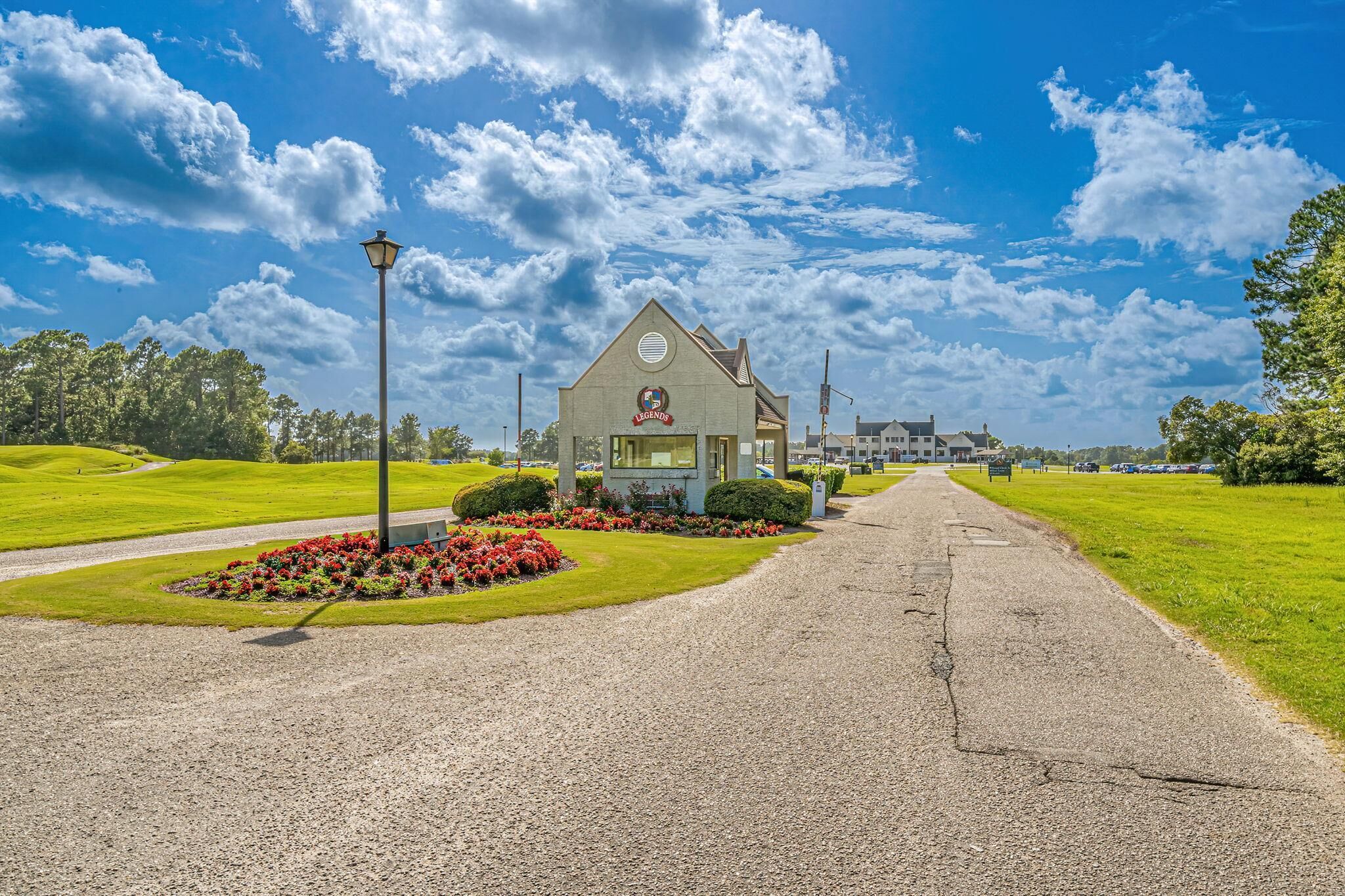 A building with a sign reading 'LEGENDS' on a gravel road with a lamppost and flower beds.