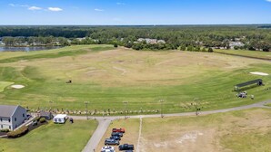 A golf course with a clubhouse, parking area, and a lake in the background. - The Victorian Golf Tee at Legends (Myrtle Beach)
