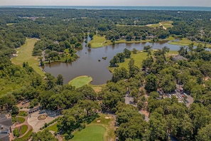 An aerial view of a golf course with multiple ponds, surrounded by dense forest.