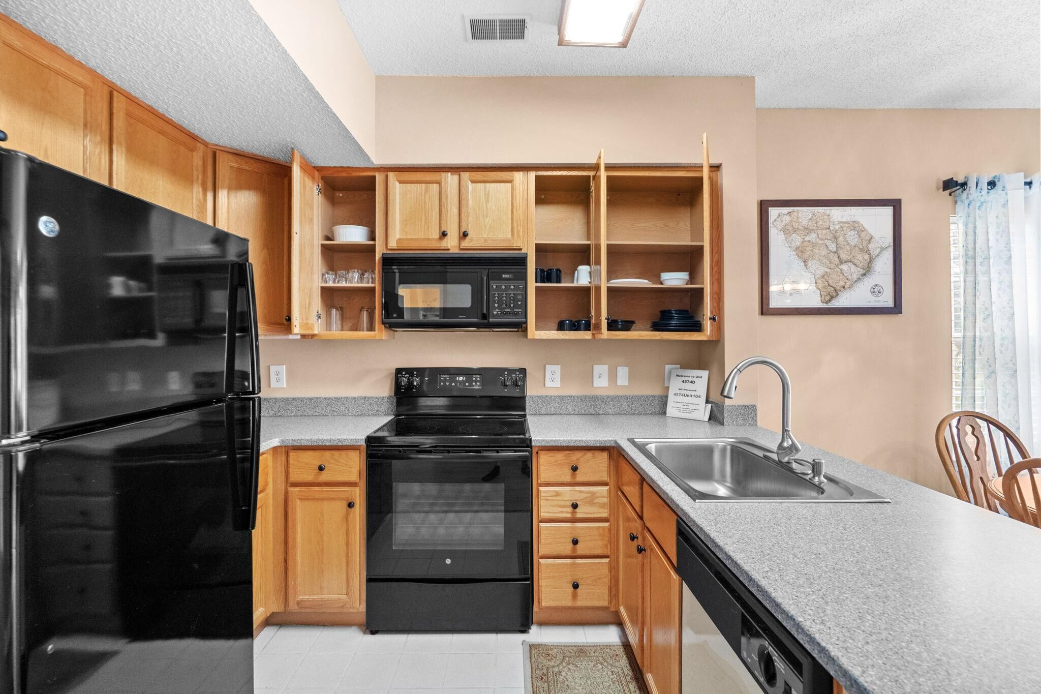 Una cocina moderna con armarios de madera, un refrigerador negro, un microondas, un horno y un fregadero.