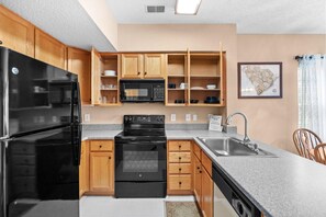A modern kitchen with wooden cabinets, a black refrigerator, a microwave, an oven, and a sink.