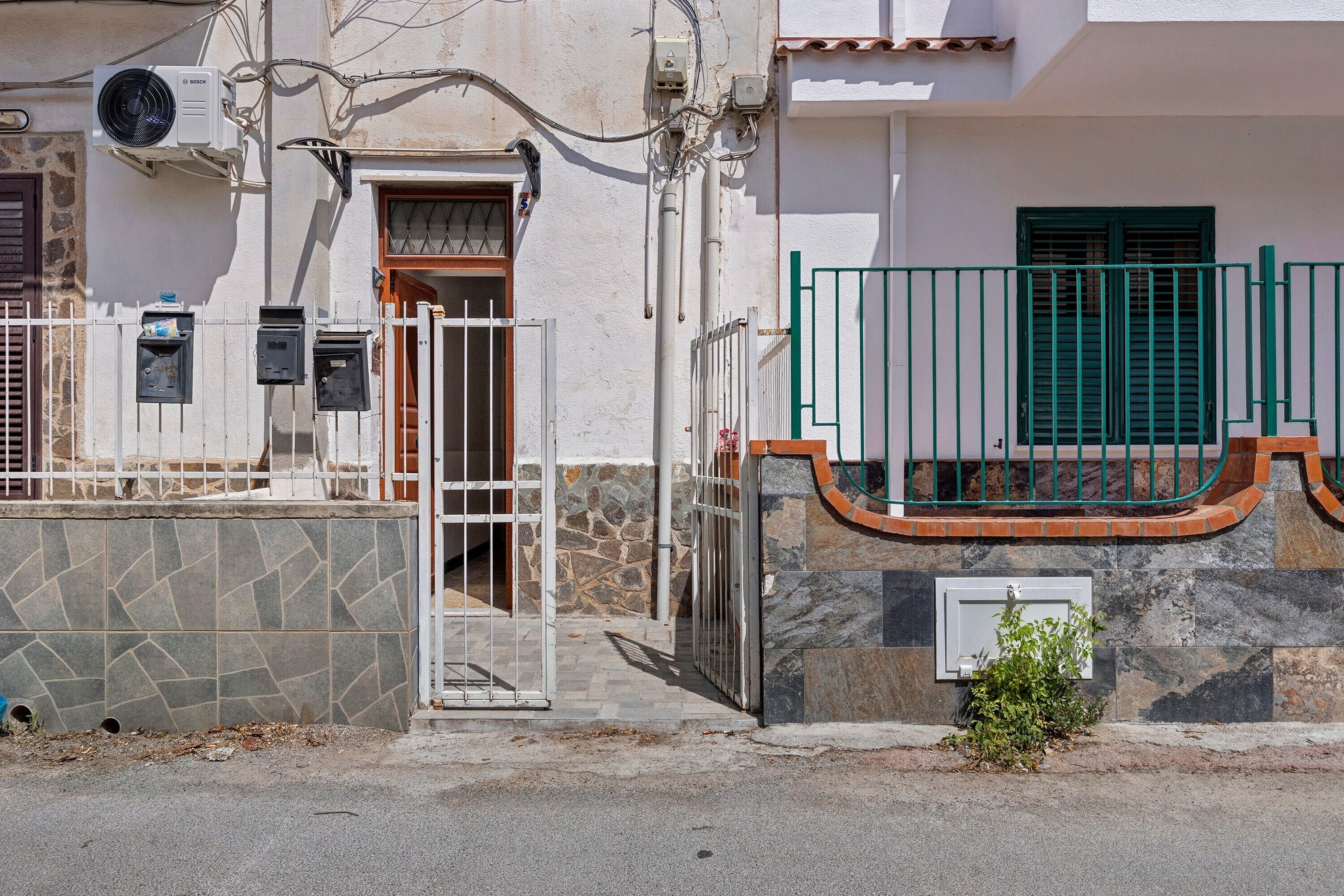 Un edificio residencial con fachada de piedra, una reja metálica y una pequeña planta verde cerca de la entrada.