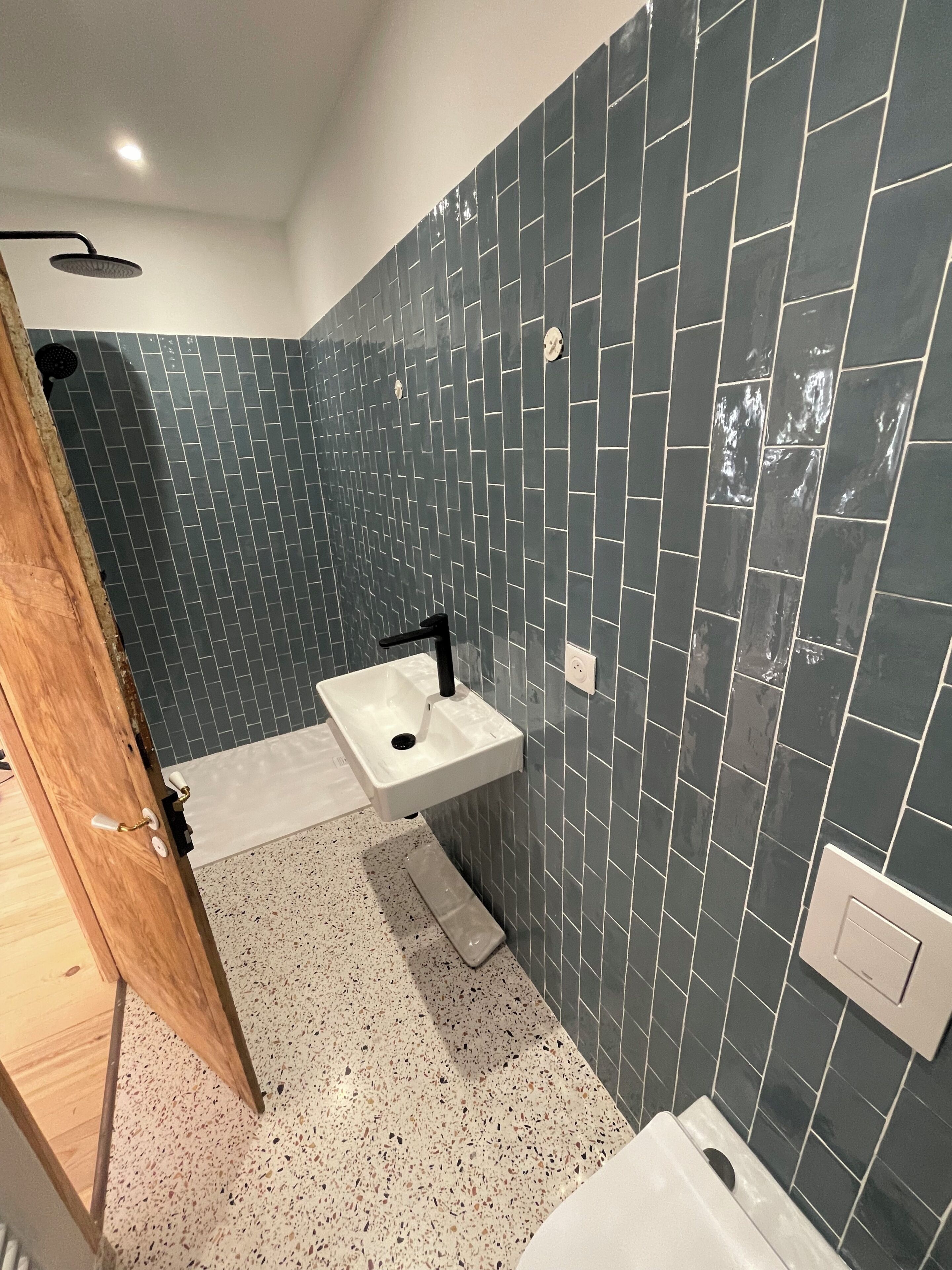 A bathroom with dark tiled walls, a white sink, and a shower area.