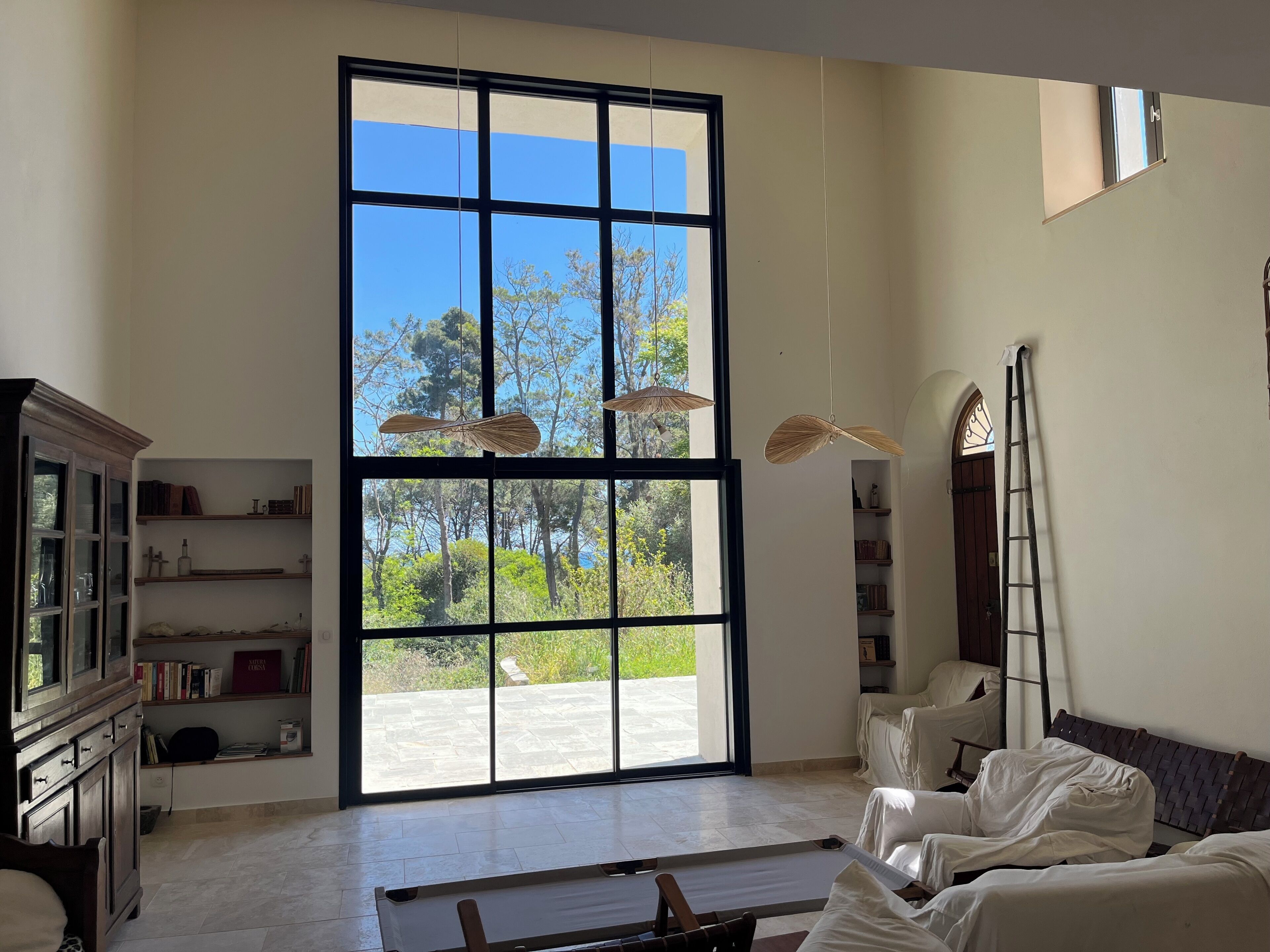 A spacious room with a large window, a wooden cabinet, a bed, and a ladder.