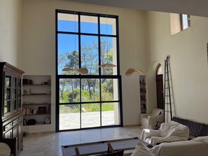 Una habitación amplia con un gran ventanal, un armario de madera, una cama y una escalera.