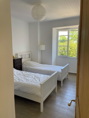 Een kamer met twee witte bedden, een vloerlamp en een raam met uitzicht op bomen.