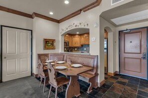 A dining area with a wooden table and bench seating, a kitchen with wooden cabinets, and a door with a handle. - Zermatt Mountain Retreat (Midway)