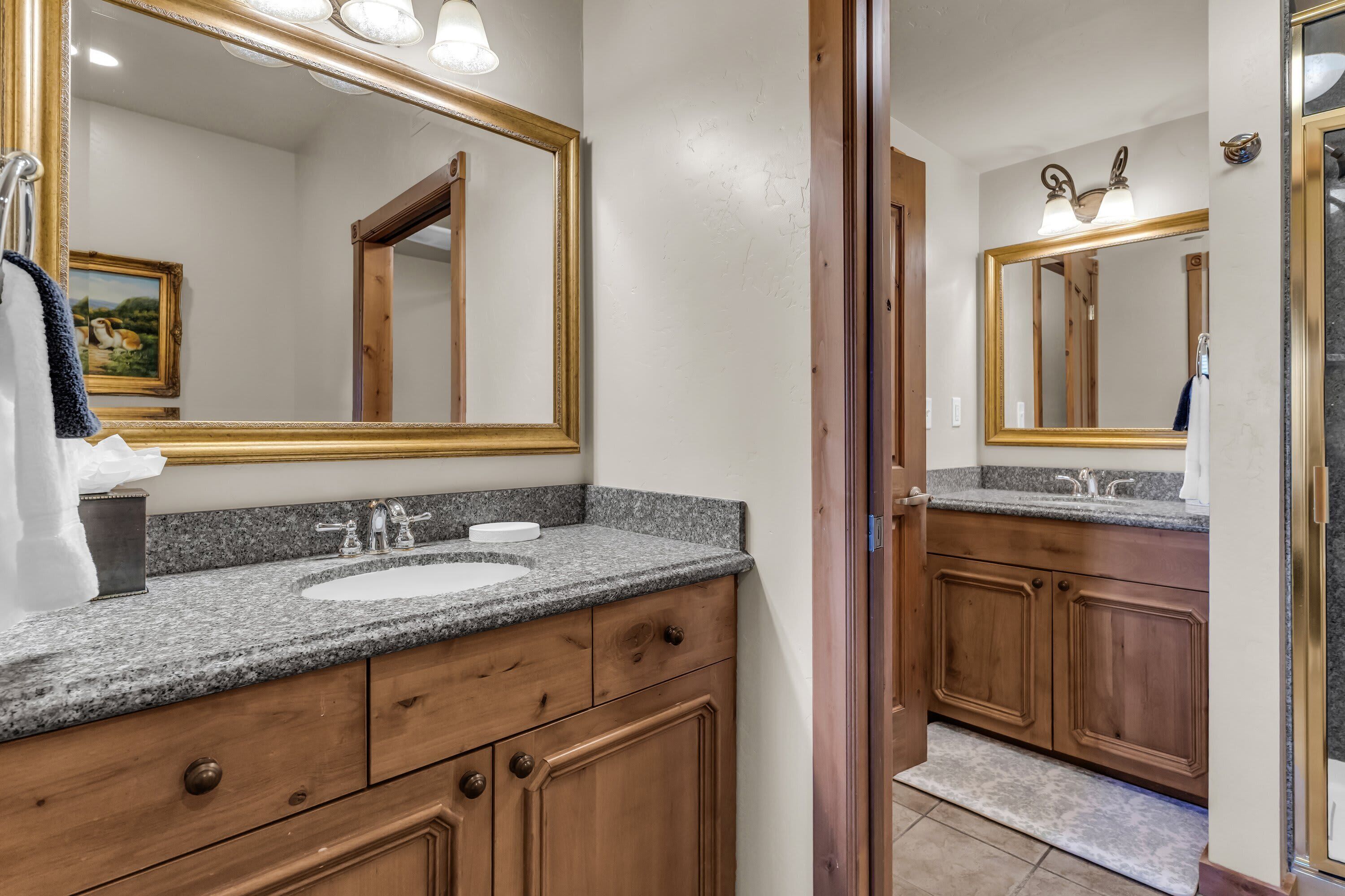 Une salle de bain avec un comptoir en granit, des meubles en bois, un grand miroir et un lavabo.