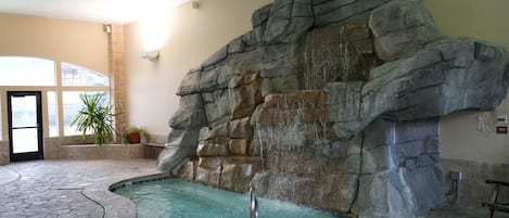 An indoor pool area with a rock wall, a hot tub, and a tiled floor.