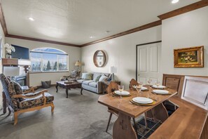 A dining area with a wooden table set for four, a sofa, and a television in the background. - Zermatt Mountain Retreat (Midway)