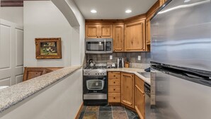 Una cocina compacta con nevera de acero inoxidable, microondas, horno y cocina a gas.