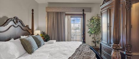 A hotel room with a large bed, a wooden wardrobe, a window with curtains, and a view of the outdoors.