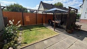A backyard with a wooden fence, a patio table with chairs, and a pergola structure. - Holiday Home Milan with Private Terrace and Garden (Holzminden)