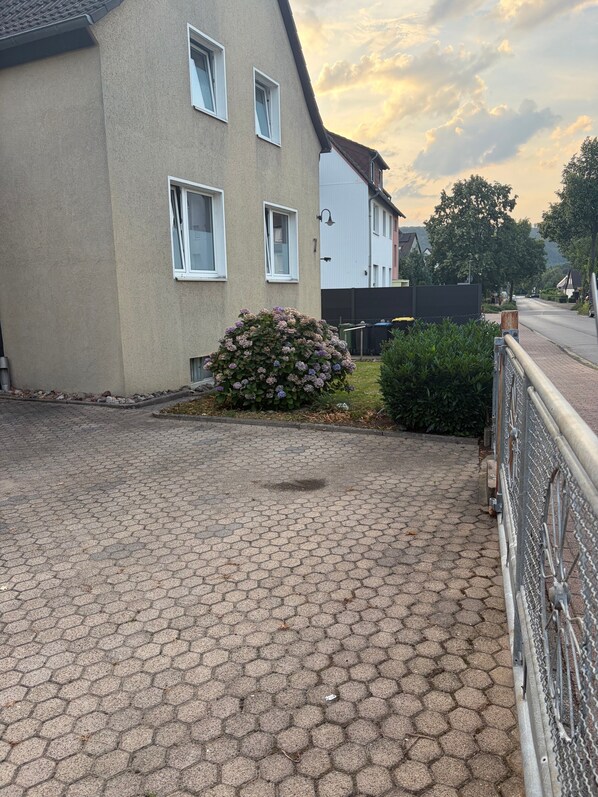A residential street with a paved driveway leading to a house with a small garden.