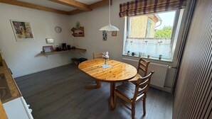 A dining area with a round wooden table, two chairs, a hanging light fixture, a window with a view, and a radiator. - Holiday Home Milan with Private Terrace and Garden (Holzminden)