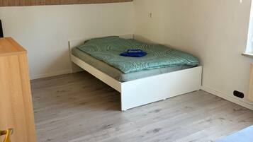 A room with a sloped ceiling, a bed with a green mattress, a wooden nightstand, and a window.