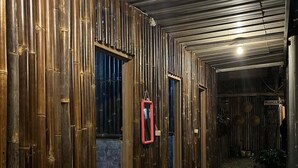 Um corredor com paredes de bambu e chão de cascalho, levando a um quarto com uma placa que diz 'MUSHROOM'.