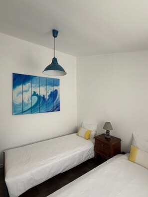 A room with two beds, a wall-mounted artwork of waves, a hanging lamp, and a nightstand with a lamp. - Monte Alentejano in Odemira, featuring a secluded house on private property. (Odemira)