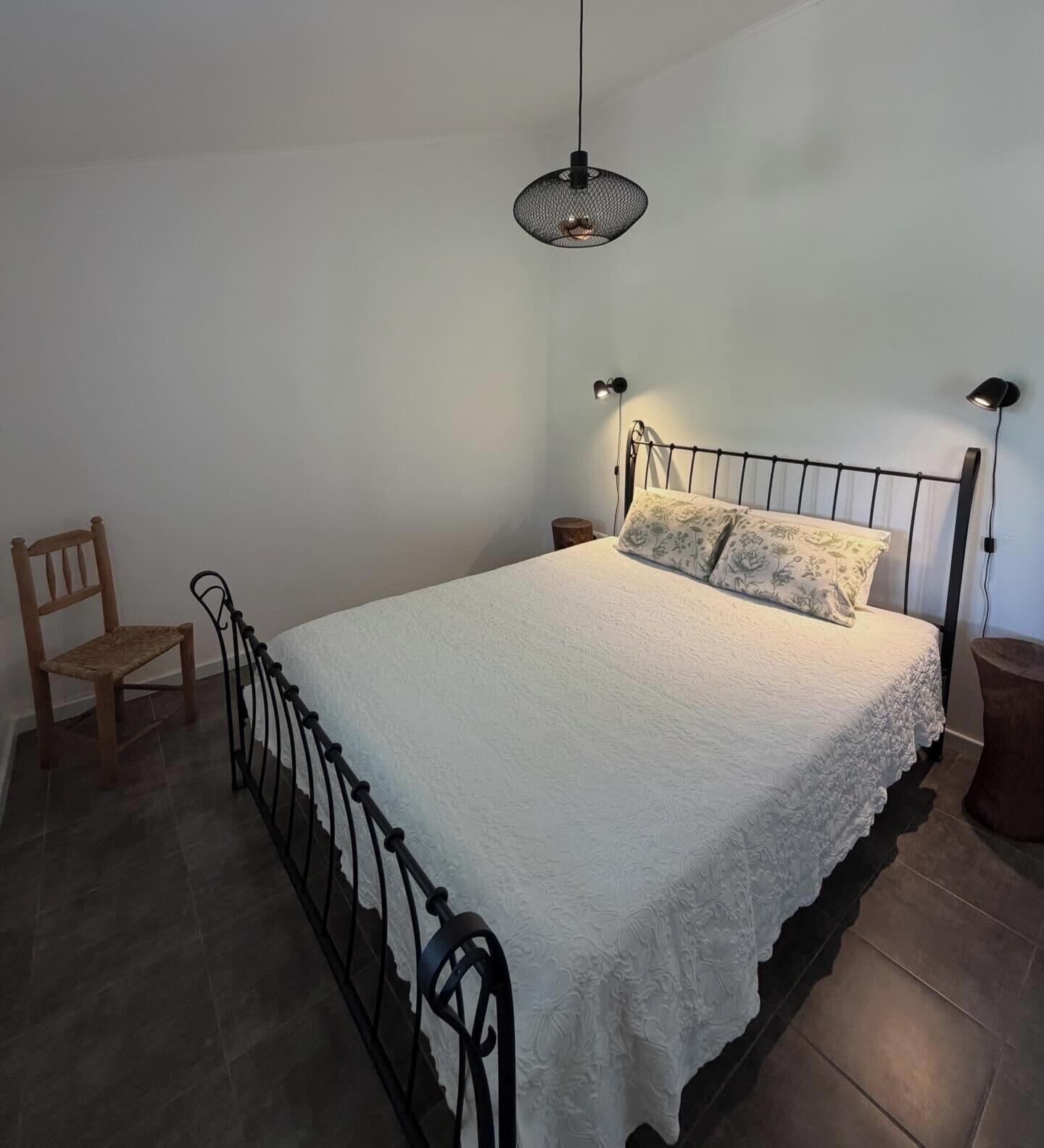Ein Schlafzimmer mit einem Bett, einem Sessel, einem Nachttisch und einer Wandlampe.