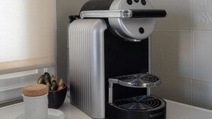 Nespresso-kahvinkeitin keittiön työtasolla, sen vieressä kahvikuppi ja pieni kulho, jossa on kahvipapuja.