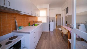 Pieni, käytännöllinen keittiö, jossa on valkoiset kaapit, liesi ja pesuallas.
