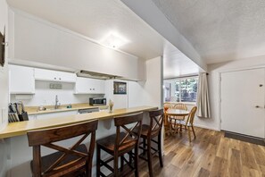 A compact kitchen with a wooden bar counter, a microwave, and a dining area with a round table and chairs. - Your Tahoe Adventure Basecamp Near Heavenly — Midweek Discounts (South Lake Tahoe)